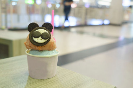 A cup of gelato with mouse-like biscuit topping served on the wooden table with blurred background.の写真素材