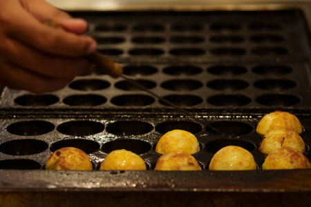 The cooking of Takoyaki. The popular Japanese street food that consists of small, ball-shaped snacks made of batter and filled with small pieces of octopus and other ingredients.の写真素材