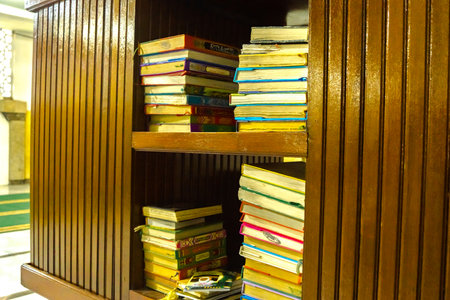 July 8, 2023. Stacks of Al Qur'an on wooden shelf in Mesjid Sunan Ample or Sunan Ample Mosque in Surabaya, Indonesia. Religious Photography.のeditorial素材