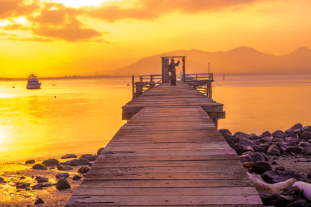A wooden pier juts out into a calm body of water, bathed in the golden light of sunrise.