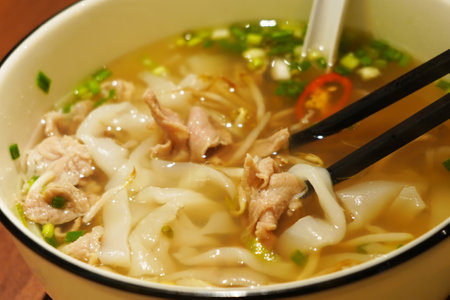 A close-up photo of a steaming bowl of pho. The broth is light brown and there are thin slices of...