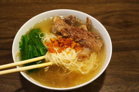 A bowl of misua or wheat vermicelli with beef tendon. The chopsticks resting on the rim. The noodles are a light brown color.の写真素材