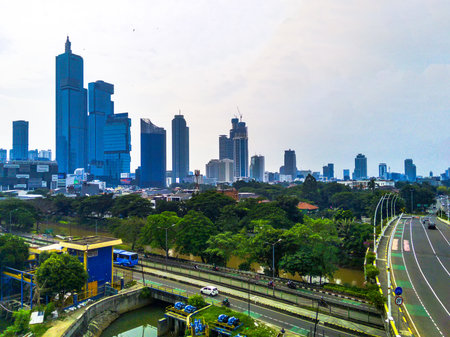 A bridge with cars traverses a river in Kuningan, Jakarta, Indonesia. The cityscape rises in the...