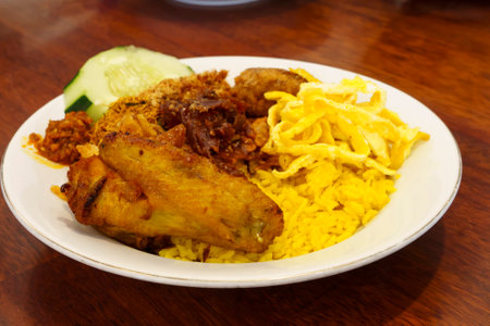 A plate of Nasi Kuning, a traditional Indonesian yellow rice dish with turmeric rice, chicken, tempeh, sambal, and other side dishes.の写真素材