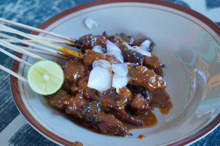 A plate of savory satay skewers with a side of lime and red onions, drizzled with a rich peanut...