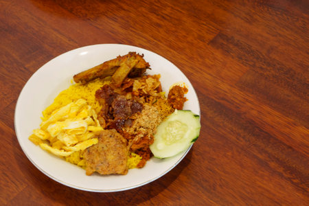 A plate of Nasi Kuning, a traditional Indonesian yellow rice dish with turmeric rice, chicken, tempeh, sambal, and other side dishes.の写真素材