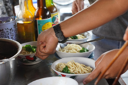 A close-up shot of Tukang Mie Ayam or a noodle vendor preparing multiple servings of chicken noodle...