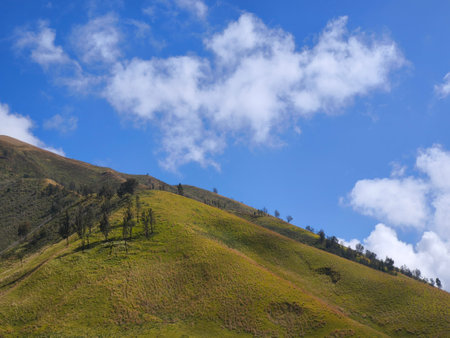 A picturesque landscape of rolling hills with vibrant green grass under a dramatic blue sky and fluffy white clouds.の写真素材