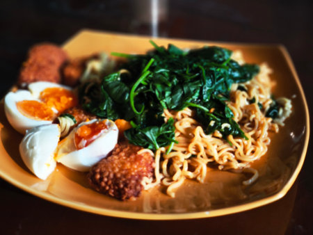 A plate of instant noodles topped with spinach, hard-boiled eggs, and fried fish cakes.の写真素材