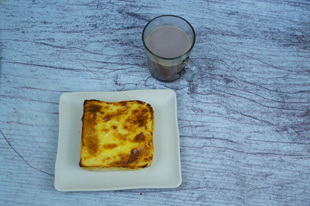 Hot chocolate and toast with cream on a white plate on a wooden tableの写真素材