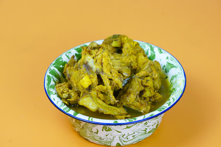 A vibrant bowl of Indonesian soto tulang ayam or chicken bones spicy soup, rich in yellow spices,...