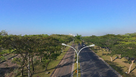 An aerial view of a wide, multi-lane road flanked by trees, with cars and motorbikes driving on a...