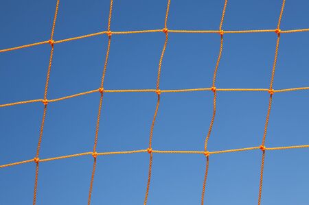 Orange soccer goal net against blue skyの写真素材