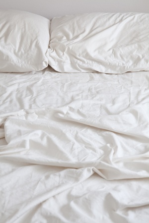 Empty bed with disheveled pillows and sheetsの写真素材