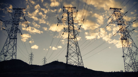 High voltage power lines and towers in silhouette against sunset sky and clouds