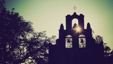 Spanish Mission Espada church bells in silhouette as the sun sets behind mission in San Antonio, Texasの写真素材