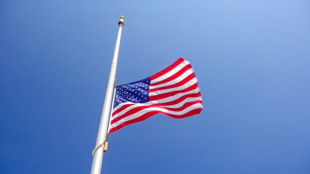 American flag flying at half mast aka half staff against a clear blue skyの写真素材