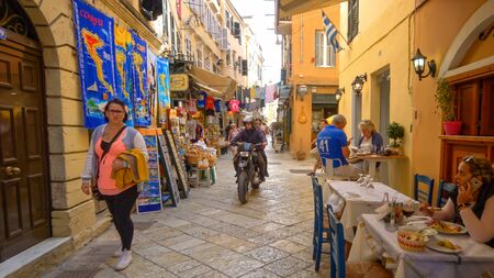 People shopping and eating on a narrow street in old town Corfu, Greeceのeditorial素材