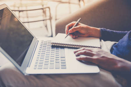Business man working on laptop computer and writing notebook in late afternoon, close up, vintage...