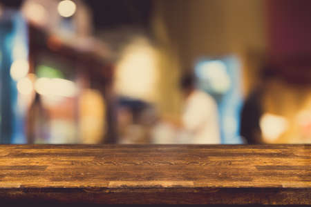 Empty dark wood table top and blur of cafe or restaurant in dark night background. For montage...