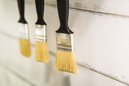 Selective focus 35 mm. hang paint brushes on white wall in a workshop.