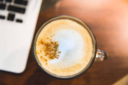 Cappuccino cup and laptop on wooden table. Above view.の写真素材