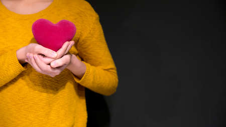 Asian woman hand hold red heart pillow with yellow sweater. Valentine concept. copy spaceの写真素材