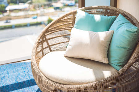 Round wicker wood chair with white cushion and comfort pillows. Near by the window and the common...
