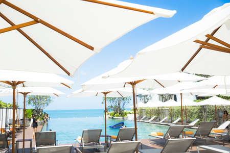 Peopple relaxing and enjoy a luxury infinity swimming pool in the beach hotel resort with the pool bed side and white vintage umbrellas.のeditorial素材