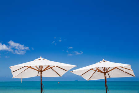 Two standing white vintage umbrellas with lanscape of beautiful blue sky and the sea. Summer vacation concept.の写真素材