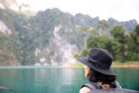 Traveler woman wearing big black hat and backpack looking at destinations sea beach. Summer holiday and vacation tripの写真素材