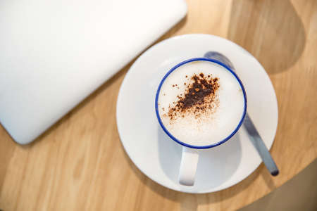 laptop with fresh cup of coffee, top view. Close up hot cappuccino coffee cup  near laptop on wood table at cafe,food and drinkの写真素材