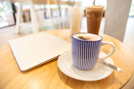 laptop with fresh cup of coffee, top view. Close up hot cappuccino coffee cup  near laptop on wood table at cafe,food and drinkの写真素材