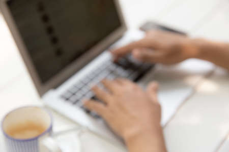 A man is working by using a laptop computer on white vintage wooden table and a cup of coffee in the table.  With hands typing on a keyboard.の写真素材