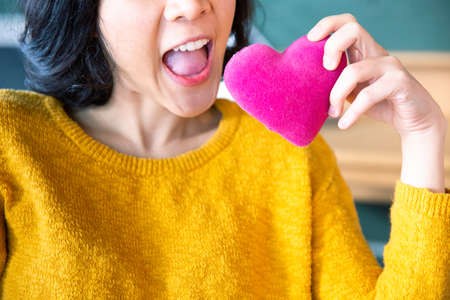Young asian woman making air bite with pink pillow heart shape.の写真素材