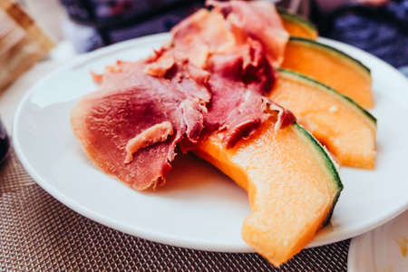 Concept of italian food with melon and prosciutto. Parma ham serving on the the white plate in italian restaurant.の写真素材