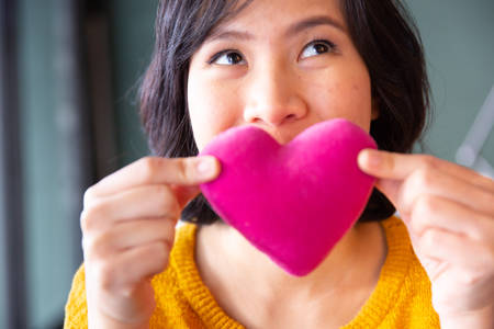 Young asian woman making air kiss with pink pillow heart shape.の写真素材