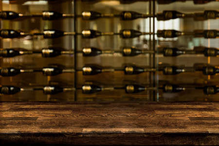 Empty wooden bar counter with defocused background Many glass of wine or champagne bottles on shelves for mock up or copy space for product presentationの写真素材