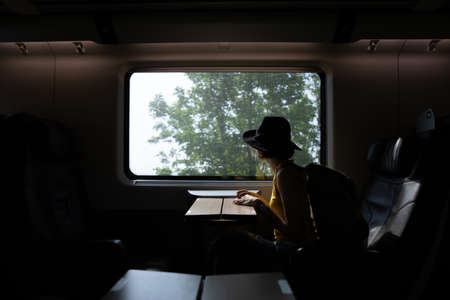 A beautiful hipster asian woman travelling on the train. Sitting on the black leather cozy comfort seat in the business class boky of the train in Europe. Tourist travel concept.の写真素材
