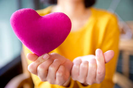 Female hands giving red heart pillow and mini heart- safety concept. Vintage filter.の写真素材