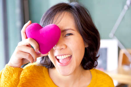 Young cute asian woman with pink heart-shaped pillow and gifts for Valentine's Day.の写真素材