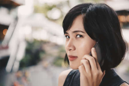 Angry asian woman talking her mobile phone in the mall with a bitchy face. Technology communication concept.の写真素材