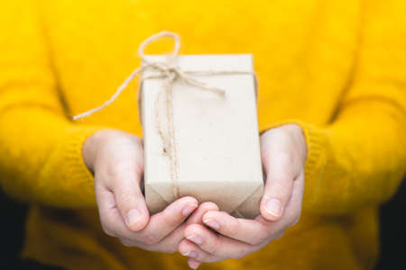 Young woman in yellow swether holding gift box for spacial event. Christmas, birthday, valentine's background concept.の写真素材