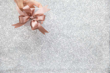 Female hands holding or giving a small gift box with copy space for text and silver glitter background.の写真素材