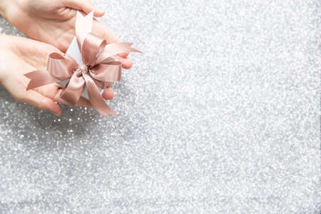Female hands holding or giving a small gift box with copy space for text and silver glitter background.の写真素材