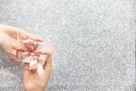 Female hands holding or giving a small gift box with copy space for text and silver glitter background.の写真素材