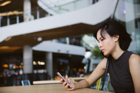 Young Asian Girl using smart phone in the shopping mall. Copy space for text and background. ...