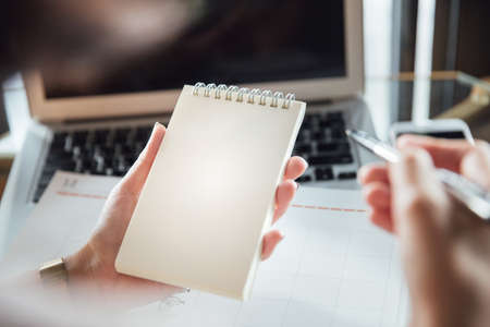 close up of business woman's hands using laptop and writing in notepad. Working on project concept.の写真素材