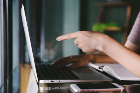 Beautiful young Asian woman working at a coffee shop with computer laptop. Pointing to the important information detail. Female freelancer connecting to internet via computer. Casual Thinking Browsing Concept.の写真素材