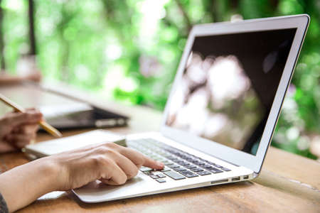 Young business woman in casual dress sitting at table in cafe and writing in notebook. On table is laptop, smartphone and cup of coffee. Freelancer working in coffee shop. Student learning online.の写真素材